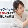 浴室で女性がシャワーヘッドとホースの接続部分を確認している様子。TOTOシャワーヘッドの交換可否と外し方を解説